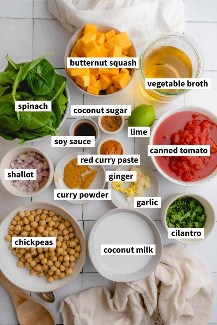 Ingredient collage of everything you need to make butternut squash curry with chickpeas, coconut milk, spinach, red curry paste, ginger and garlic. Each ingredient is labelled.