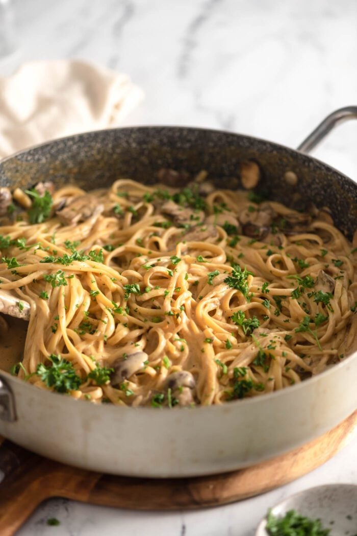 Creamy vegan carbonara pasta with fresh parsley in a large skillet sitting on a cutting board.