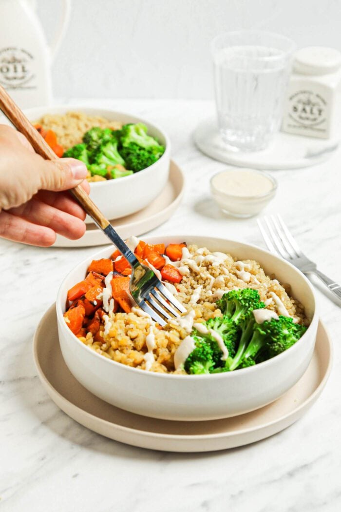 Hand using a fork to dig into a healthy lentil and quinoa bowl with roasted squash and broccoli.