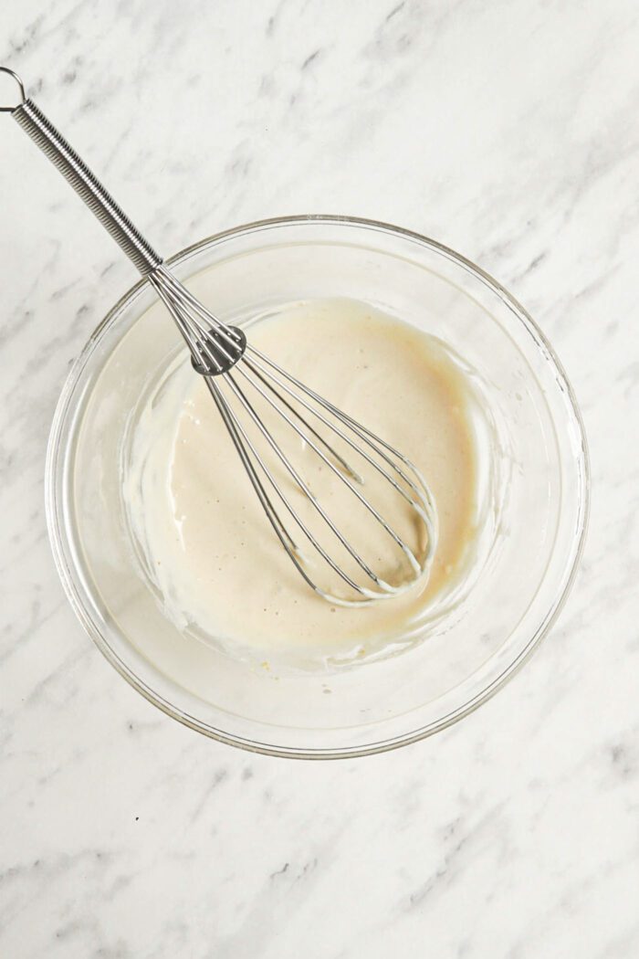 Creamy tahini sauce in a glass mixing bowl with a metal whisk.