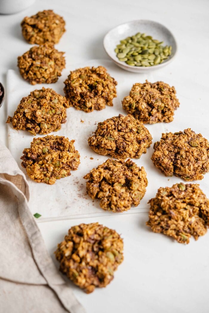 A number of sweet potato cookies on a piece of parchment paper beside a small dish of pumpkin seeds.