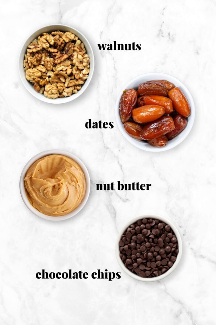 Walnuts, dates, peanut butter and chocolate chips each in a bowl. Each ingredient is labelled with text.