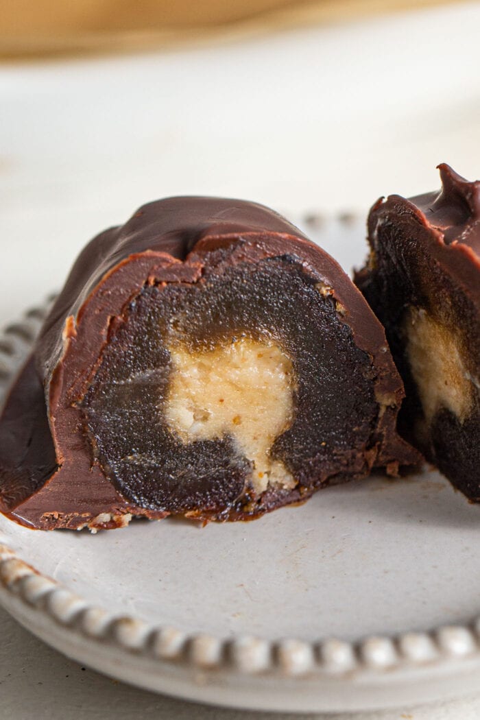 Close up of a cut open chocolate-covered medjool date with a peanut butter filling on a small plate.