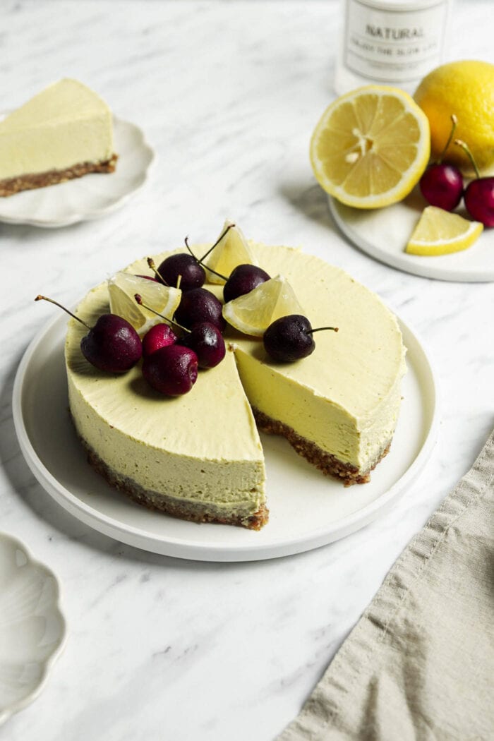 Lemon cheesecake topped with cherries with a slice cut out of it.
