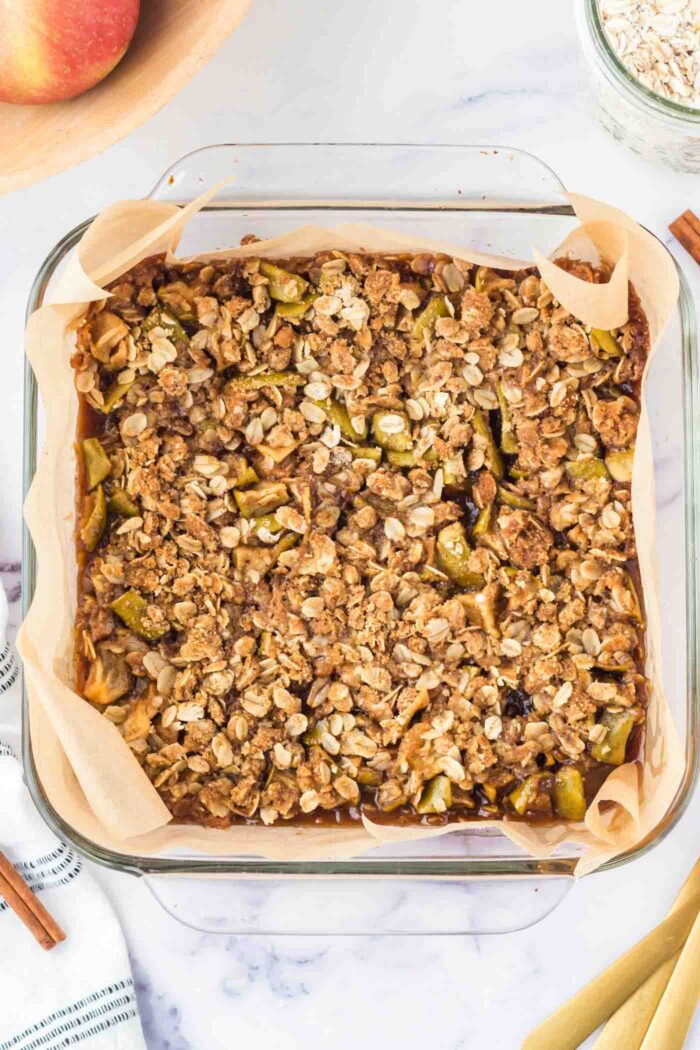 Baked apple crumble bars in a glass baking dish lined with parchment paper.