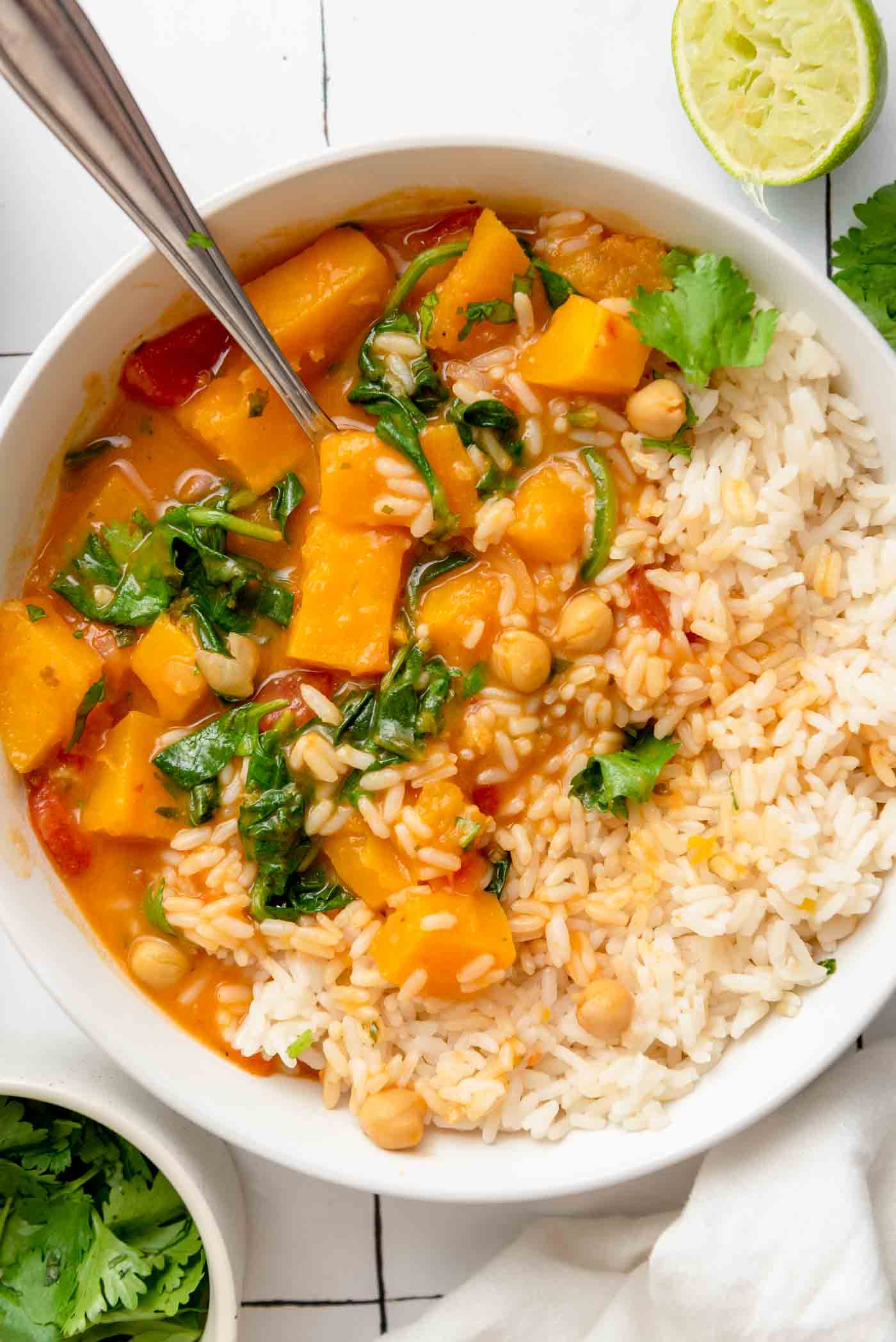 Bowl of creamy butternut squash curry with chickpeas and spinach served with rice.