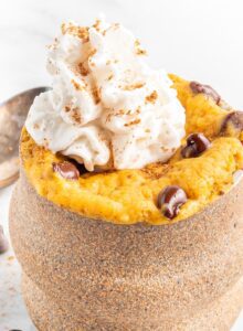 Close up of a pumpkin mug cake with chocolate chips and whipped cream.