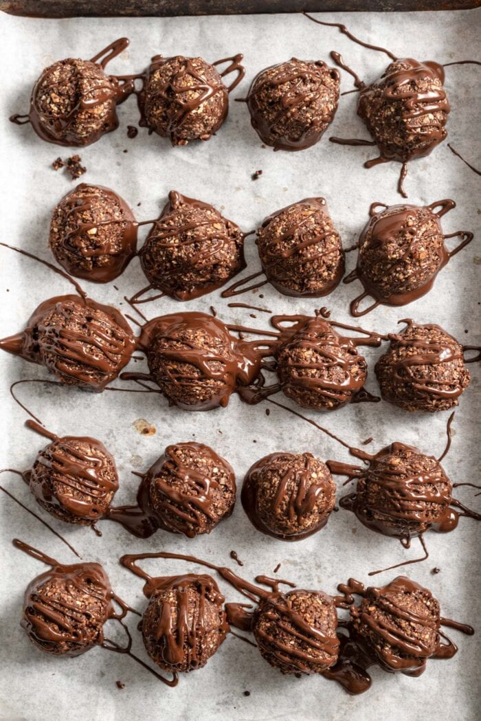 Baking tray of chocolate macaroons covered in drizzled melted chocolate.
