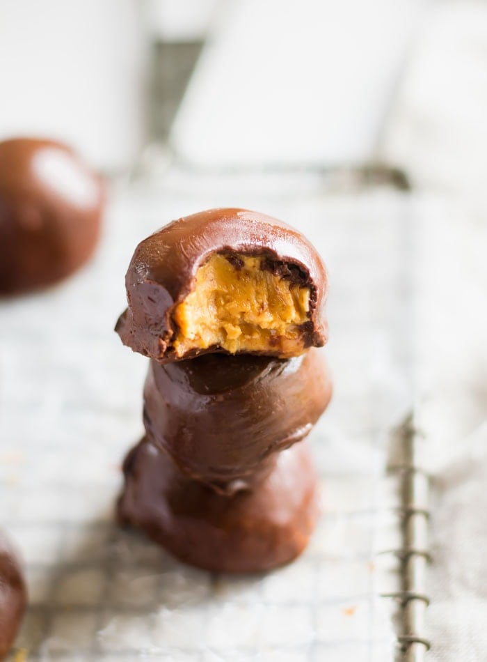 A stack of 3 chocolate-covered peanut butter balls. The one on top has a bite out of it.