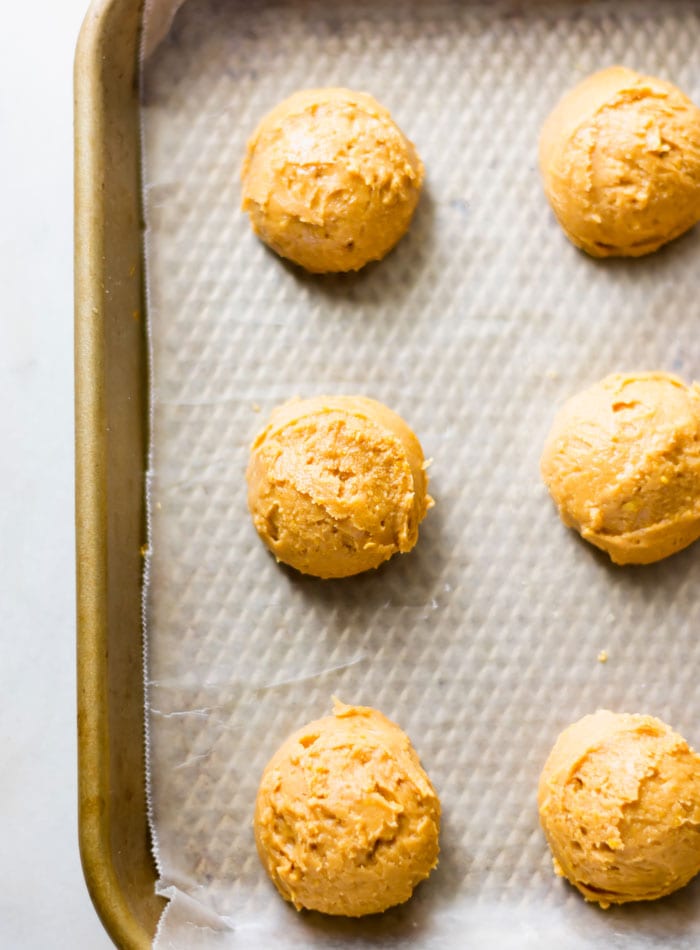 Balls of peanut butter dough on a baking tray lined with parchment.