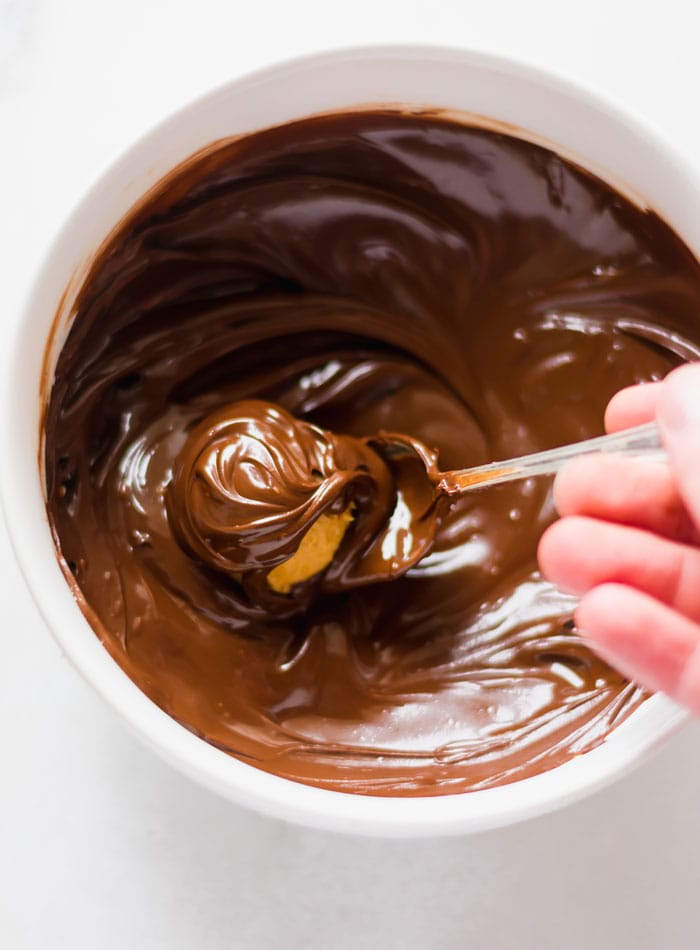 A peanut butter ball being dipped in a bowl of melted chocolate.