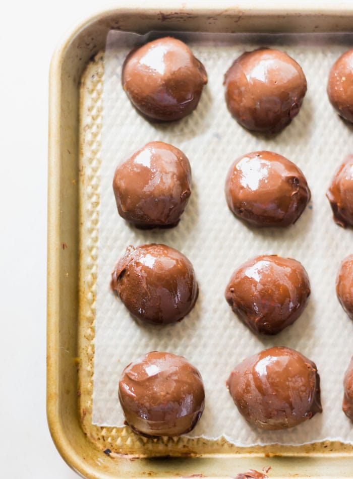 8 chocolate-coated balls sitting on a small baking sheet lined with parchment paper.