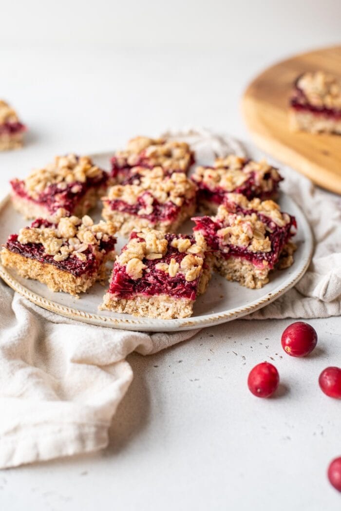A plate of cranberry oat bars with some whole cranberries scattered around.