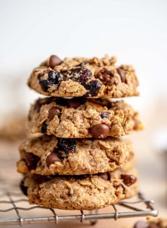 Stack of 4 oatmeal cookies with cranberries, walnuts and chocolate chips in them sitting on the edge of a wire baking rack.