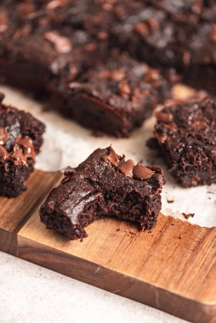 A chocolate chip zucchini brownie with a bite out of it on a cutting board with more brownies in the background.