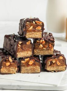 Stack of homemade Snickers bars with a cookie base, caramel layer and chocolate coating.