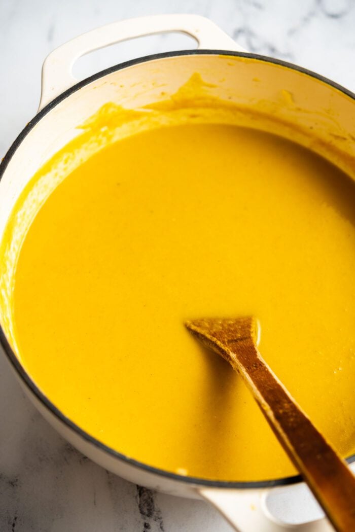 A large pot of creamy squash soup with a wooden spoon resting in the pot.