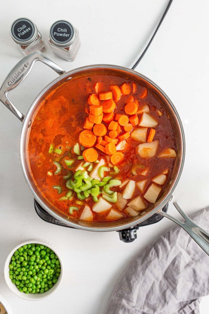Tomato broth with chopped carrots, peas and potato cooking in a skillet.
