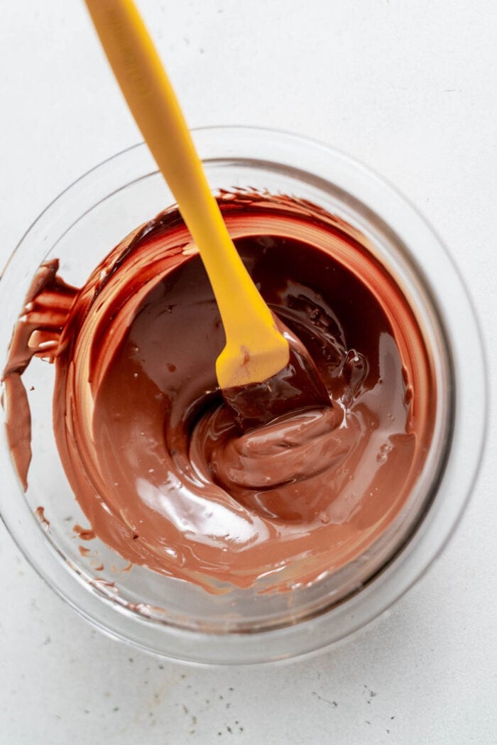 Melted chocolate in a glass mixing bowl with a spatula.
