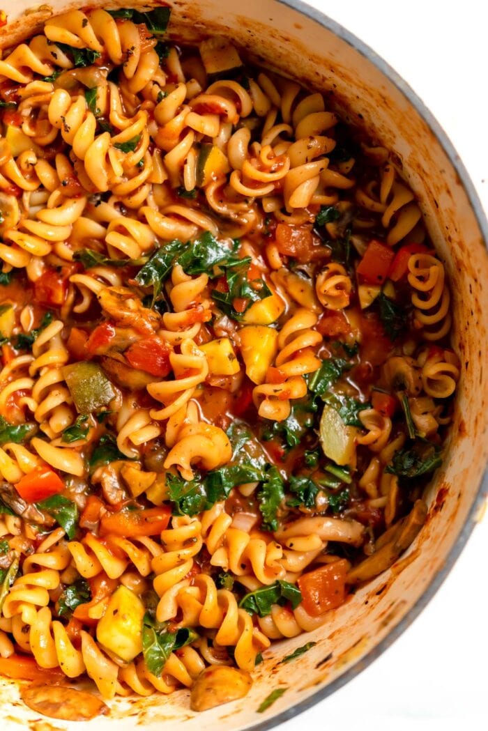 A large pot of rotini pasta, kale and chopped mushroom, bell pepper and onion in tomato sauce.