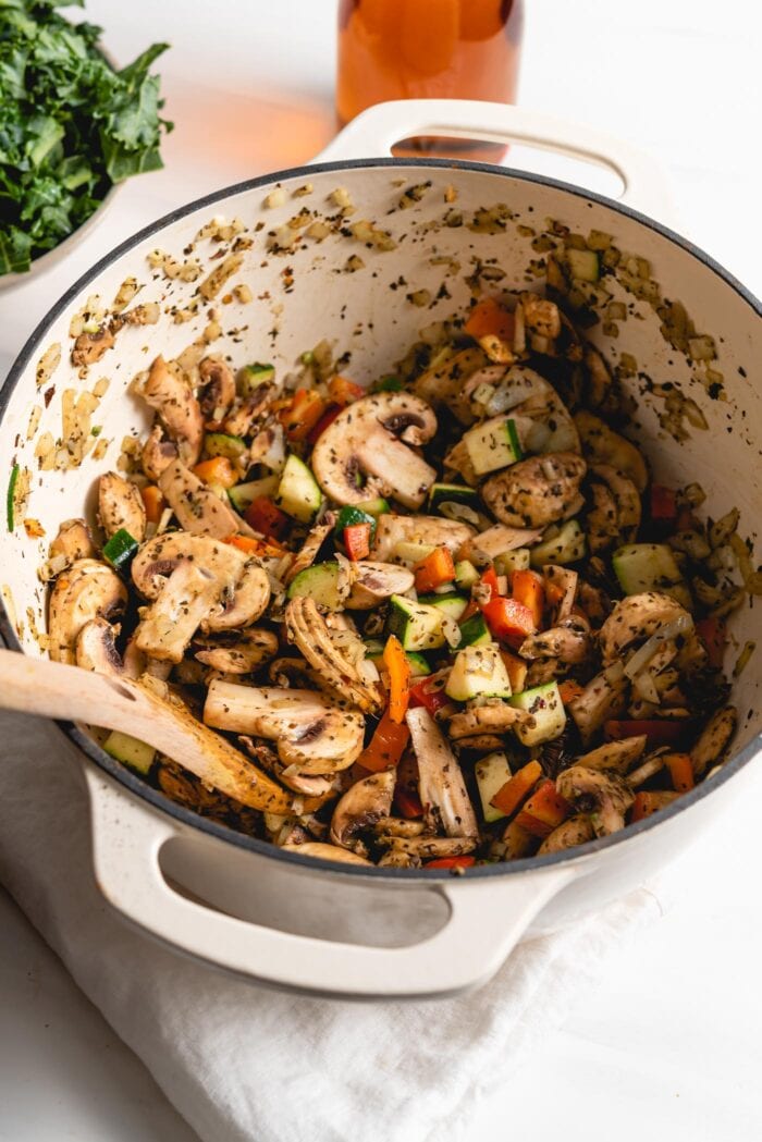 Chopped mushrooms, bell peppers and zucchini cooking in a large pot.