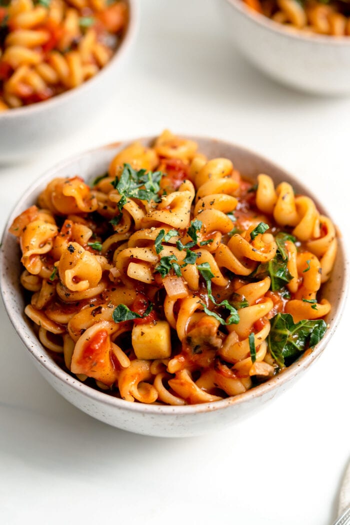 Bowl of pasta noodles with tomato vegetable sauce and fresh chopped herbs on top.