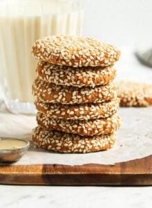 Stack of 5 tahini cookies on a cutting board with a glass of milk behind them.