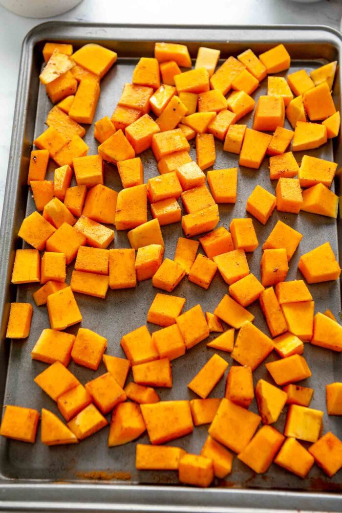 Cubes of butternut squash tossed in spices on a baking sheet.