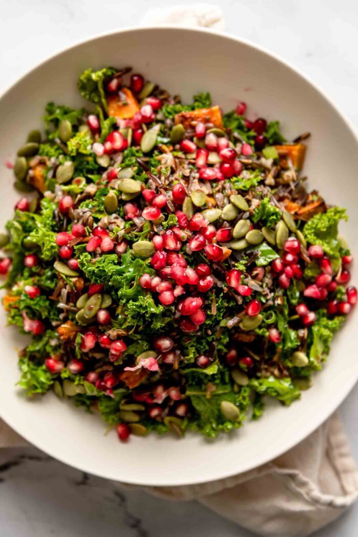 Overhead view of a holiday-inspired wild rice salad with pomegranate arils, pumpkin seeds, kale and cubes of roasted butternut squash in a bowl.